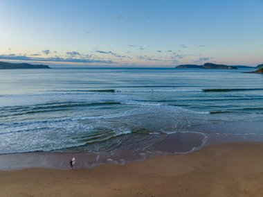 Güneş doğarken küçük dalgalar ve çoğunlukla açık gökyüzü ile Central Coast, NSW, Avustralya 'daki Umina Sahili' nde.