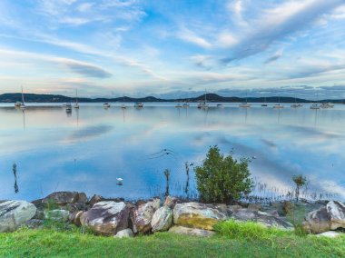 Central Coast, NSW, Avustralya 'daki Koolewong ve Tascott' ta tekneler, bulutlar ve yansımalarla yumuşak mavi bir gün batımı..