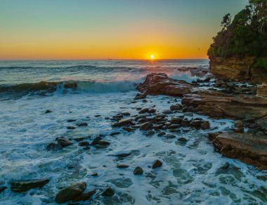 Central Coast, NSW, Avustralya 'daki Avoca Sahili' nde sörfçülerle ve kayalarla gün doğumu deniz manzarası.
