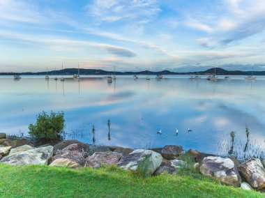 Central Coast, NSW, Avustralya 'daki Koolewong ve Tascott' ta tekneler, bulutlar ve yansımalarla yumuşak mavi bir gün batımı..