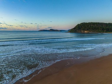 Güneş doğarken küçük dalgalar ve çoğunlukla açık gökyüzü ile Central Coast, NSW, Avustralya 'daki Umina Sahili' nde.