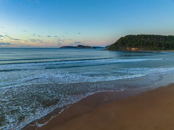 Güneş doğarken küçük dalgalar ve çoğunlukla açık gökyüzü ile Central Coast, NSW, Avustralya 'daki Umina Sahili' nde.