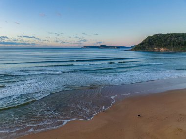 Güneş doğarken küçük dalgalar ve çoğunlukla açık gökyüzü ile Central Coast, NSW, Avustralya 'daki Umina Sahili' nde.