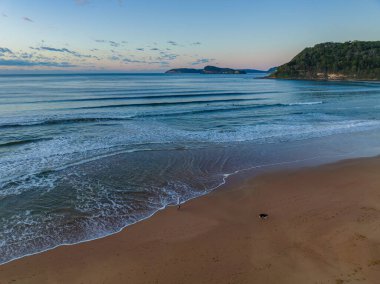 Güneş doğarken küçük dalgalar ve çoğunlukla açık gökyüzü ile Central Coast, NSW, Avustralya 'daki Umina Sahili' nde.