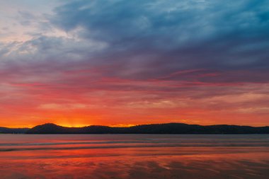 Sunrise at the beach with colourful high cloud filled sky and flat surf at Umina Point, Umina Beach on the Central Coast, NSW, Australia.