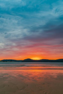 Sunrise at the beach with colourful high cloud filled sky and flat surf at Umina Point, Umina Beach on the Central Coast, NSW, Australia.