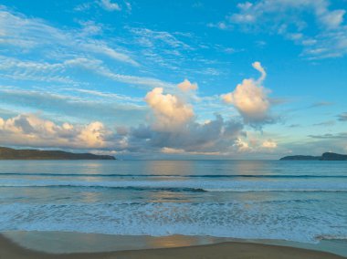 Central Coast, NSW, Avustralya 'daki Umina Sahili' nde küçük dalgalar ve yağmur bulutlarıyla gün batımı deniz manzarası..