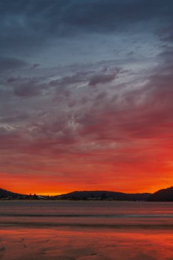 Sunrise at the beach with colourful high cloud filled sky and flat surf at Umina Point, Umina Beach on the Central Coast, NSW, Australia.