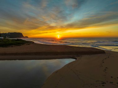 Avoca Lagoon ve Avoca Sahili 'ndeki NSW, Avustralya' daki Avoca Sahili 'nde bulutlu ve yumuşak denizli hava gündoğumu.