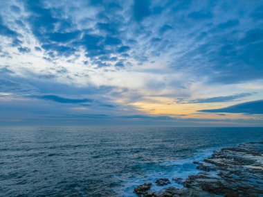 Sunrise seascape with high cloud, rocks and small waves at Avoca Beach on the Central Coast, NSW, Australia.