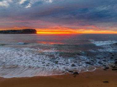 Aerial sunrise with medium and high cloud filled sky with small waves at  Macmasters Beach on the Central Coast, NSW, Australia.