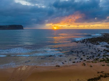 Orta Sahildeki Macmaster Sahili 'nde yağmur bulutları ve küçük dalgalarla hava gündoğumu, NSW, Avustralya.