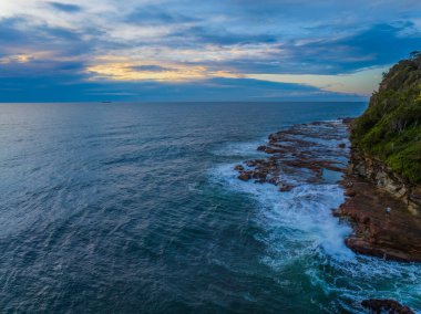 Sunrise seascape with high cloud, waves and surfers at Avoca Beach on the Central Coast, NSW, Australia.