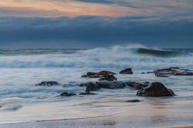 Winter sunrise at the seaside with soft cloud covered sky and waves rolling in at Killcare Beach on the Central Coast, NSW, Australia.