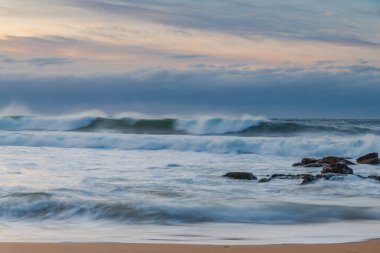Winter sunrise at the seaside with soft cloud covered sky and waves rolling in at Killcare Beach on the Central Coast, NSW, Australia.