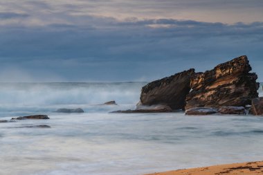 Sahil kıyısında kış gündoğumu, yumuşak bulutlarla kaplı gökyüzü, kayalar ve dalgalar Central Coast, NSW, Avustralya 'daki Killcare Sahili' nde akıyor..