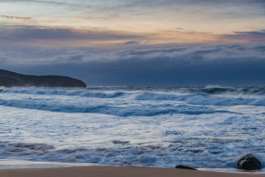 Winter sunrise at the seaside with soft cloud covered sky and waves rolling in at Killcare Beach on the Central Coast, NSW, Australia.