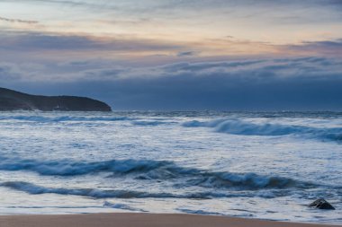 Winter sunrise at the seaside with soft cloud covered sky and waves rolling in at Killcare Beach on the Central Coast, NSW, Australia.