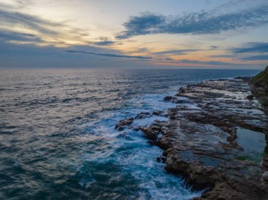 Sunrise seascape with high cloud, rocks and small waves at Avoca Beach on the Central Coast, NSW, Australia.