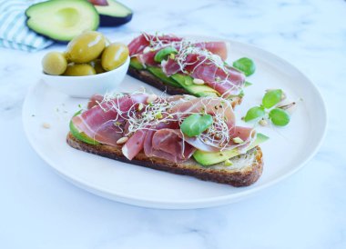 Avokado, prosciutto ya da jamon dilimli tam tahıllı sandviçler filizlenmiş tohumlar ve bitkiler. Temiz yemek, sağlıklı kahvaltı. Üst görünüm.