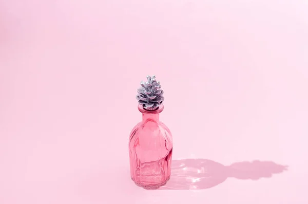 Mantar yerine gümüş kozalaklı güzel pembe bir parfüm şişesi. Noel ya da yeni yıl kutlaması hediyesi. Yıl sonu şenlikli yaratıcı konsept. Yıldönümü veya kutlama sanatsal tasarımı.