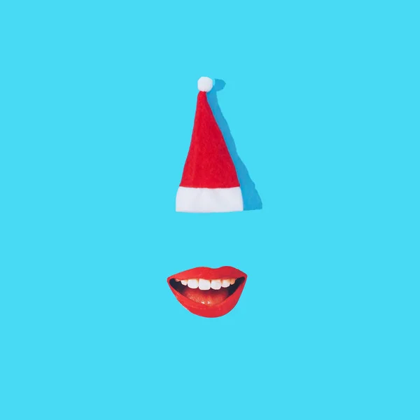 Kırmızı gülümseyen kadın dudakları ve pastel mavi arka planda Noel Baba şapkası. Minimum Noel ya da yıl sonu tatili konsepti. Moda sanatsal tasarım.