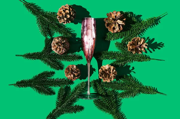 Etrafında çam ağacı dalları ve çam kozalakları olan güzel, mor bir şampanya kadehi. Noel ya da Yeni Yıl Festivali atmosferi yaratıcı kavram ya da davetiye kartı.