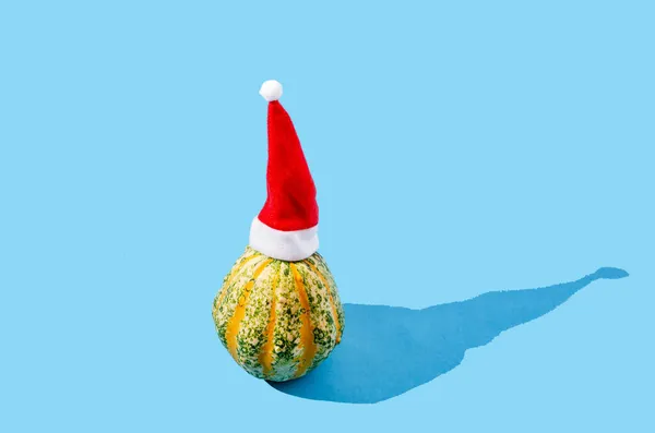 Mavi arka planda Noel Baba kırmızı şapkalı sarı yeşil bir balkabağı. Komik soğuk sonbahar hava konsepti. Cadılar Bayramı veya Şükran Günü yaratıcı tasarımı.
