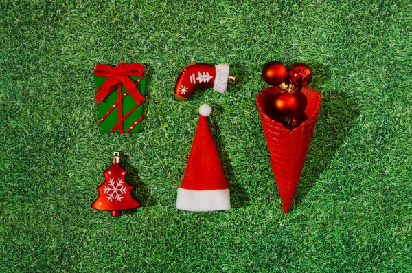 Noel süslemesinden yapılmış parlak bir bilgi ya da kalıp: bir Noel ağacı, paketlenmiş bir hediye, bir bot, Noel Baba 'nın şapkası ve arka planda yapay çimenler üzerinde kırmızı topları olan kırmızı bir dondurma külahı. Gerçeküstü yaratıcı kavramda Noel ya da Yeni Yıl sembolleri.