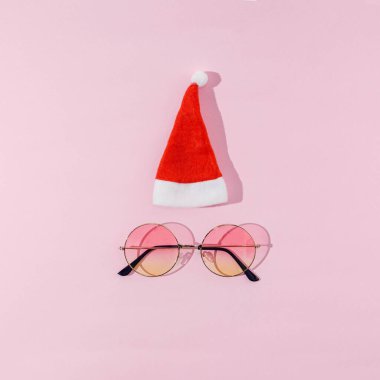 Noel Baba 'nın beyaz ponponlu kırmızı şapkası ve pastel pembe arka planda yuvarlak renkli güneş gözlüğü. Kart, pankart ya da reklam için modaya uygun ve komik bir Noel konsepti.