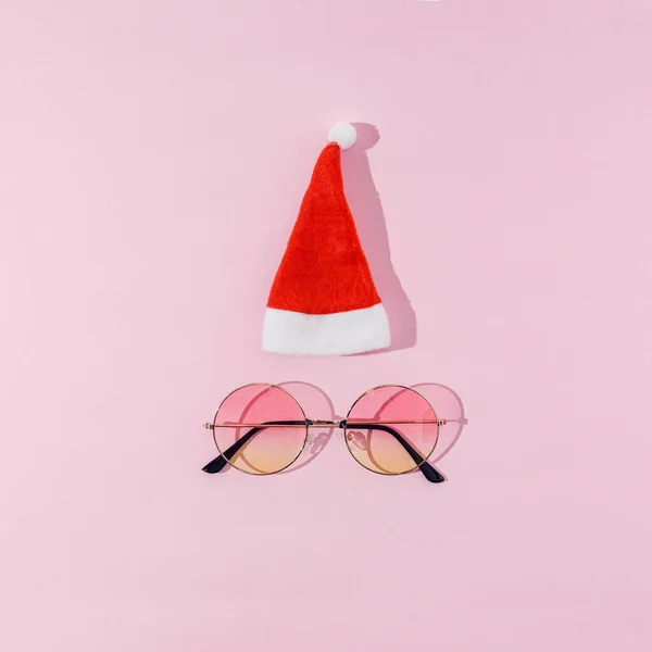 Noel Baba 'nın beyaz ponponlu kırmızı şapkası ve pastel pembe arka planda yuvarlak renkli güneş gözlüğü. Kart, pankart ya da reklam için modaya uygun ve komik bir Noel konsepti.