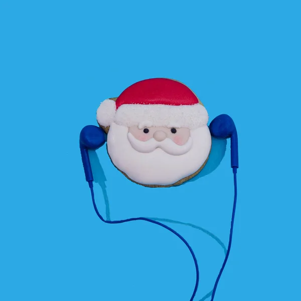 Noel Baba kafası pastel mavi arka planda mavi kulaklıklı zencefilli kekten yapılmış. Web afişi veya kart için asgari gerçeküstü yaratıcılık kavramı. Noel ya da yeni yıl partisi daveti için komik tasarım.