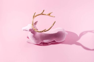 Pastel pembe arka planda altın boynuzlu pembe bir ren geyiği. Minimal kış festivali web afişi veya kart için yaratıcı sezon konsepti. Geleneksel olmayan Noel ya da Yeni Yıl sembolik tasarımı.