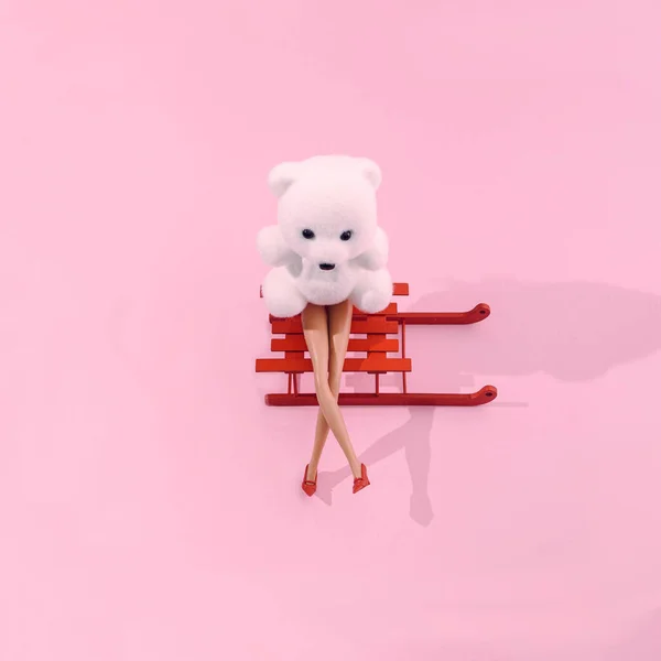 Kırmızı ayakkabılarla kırmızı kızağın üzerinde oturan beyaz bir oyuncak ayı. Pastel pembe arka plan. Kart veya web içeriği için gerçeküstü Noel ya da kış sezonu yaratıcı konsepti. Yeni yıl fantezi tasarımı.