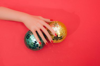 İki dev altın disko süslemesi yeşil ve kırmızı arka planda altın sarısı üzerinde kırmızı tırnaklı bir kadın eli var. Üst Manzara. Şenlikli tatiller için canlı gerçeküstü konsept.