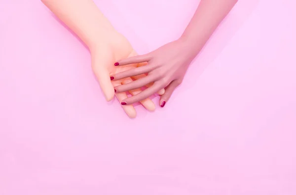 Pastel pembe arka planda kırmızı tırnaklı bir kadın eli. Sevgililer Günü afişi ya da kartı için en az yaratıcı kavram. Nişan için sanatsal tasarım ya da düğün davetiyesi. Düz yatıyordu.