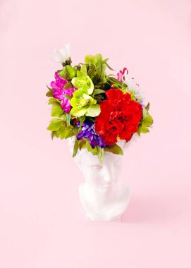 Alçıtaşından yapılmış beyaz bir antika kafa. Şapka yerine taze, renkli bir buket. Bahar sezonu kartı ya da afişi için gerçeküstü yaratıcı konsept.