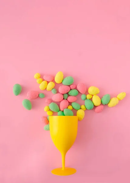 Pembe arka planda sarı, yeşil ve pembe paskalya yumurtalarıyla dolu parlak sarı bir şarap kadehi. Paskalya bayramı kartı ya da afişi için renkli yaratıcı konsept.