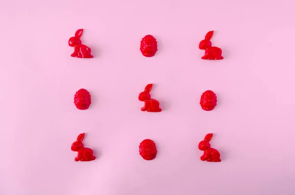 Kırmızı Paskalya tavşanları ve pastel pembe arka planda yumurtalardan yapılmış bir desen ya da duvar kağıdı. Bahar bayramı afişi veya kartı için en az simgesel yaratıcı kavram.