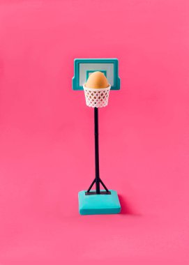 Basketbol sepetinde pembe arka planda bir Paskalya yumurtası. Festival afişi, duvar kağıdı veya kart için en az gerçeküstü kavram.