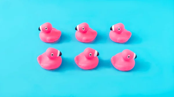 Mavi arka planda iki sıra düzgün dizilmiş pembe plastik ördek. Yaz tatili afişi ya da reklam için en az yaratıcı kavram. Boşluğu kopyala.