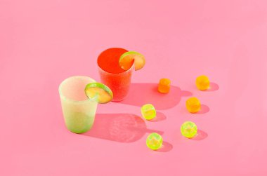 Limon yeşili ve limon dilimli turuncu bir bardak ve pembe arka planda renkli buz küpleri. Yaz afişi ya da duvar kağıdı için moder yaratıcı konsept