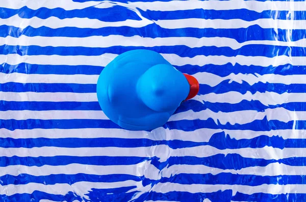 縞模様の青と白の背景に水の中に青いプラスチック製のアヒルの水泳 夏休みのレジャーのための最小限のシュールなコンセプト 平置きだ トップ表示 — ストック写真