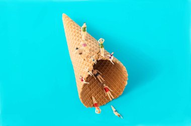 Pastel mavi arka plana karşı bir dondurma külahı ve üstünde ve külahta mini insanlar. Deniz kenarı afişlerinde yaz tatili için en az yaratıcı kavram. Gerçeküstü sanatsal tasarım