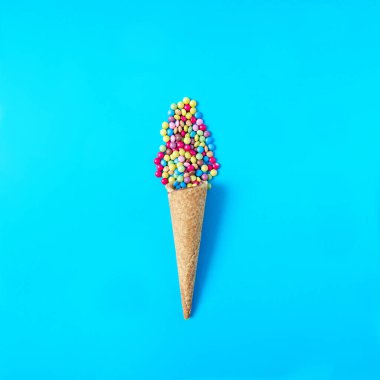 Pastel mavi arka planda küçük renkli çikolatalarla dolu bir dondurma külahı. Yaz tatili ve tatil için en az konsept. Uzayı kopyala Düz yatıyordu