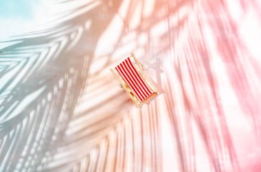 Kırmızı ve mavi palmiye yapraklarından oluşan arka planda çizgili kırmızı ve beyaz bir güneş yatağı. Yaz tatili tatil beldesi reklamı ya da afişi için en az yaratıcı kavram.