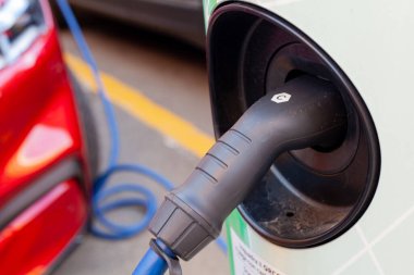 Bir şarj istasyonuna bağlı kablo, arka planda odaklı olmayan kırmızı zarif elektrikli araba