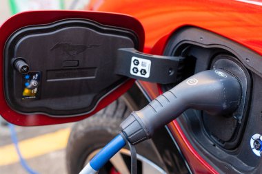 Şarj istasyonundaki kırmızı, şık bir elektrikli arabaya bağlı bir kablo.