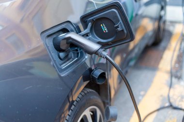 Şarj istasyonundaki gri bir elektrikli arabaya bağlı bir kablo.