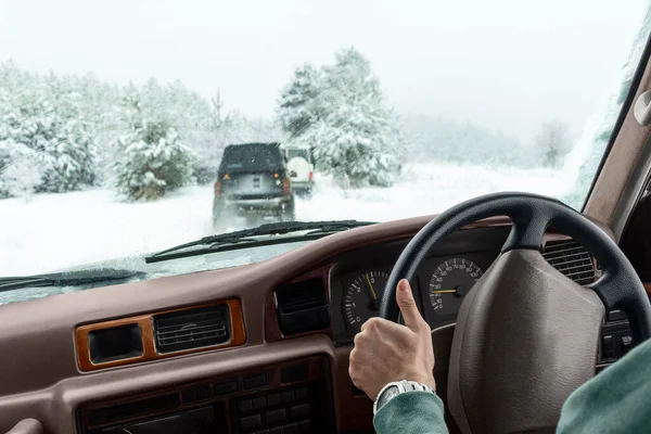 Extreme winter driving on snow off-road car travel. Hand of male driver on steering wheel of vehicle and view from auto window of suv caravans driving along wild forest road and snow-covered trees